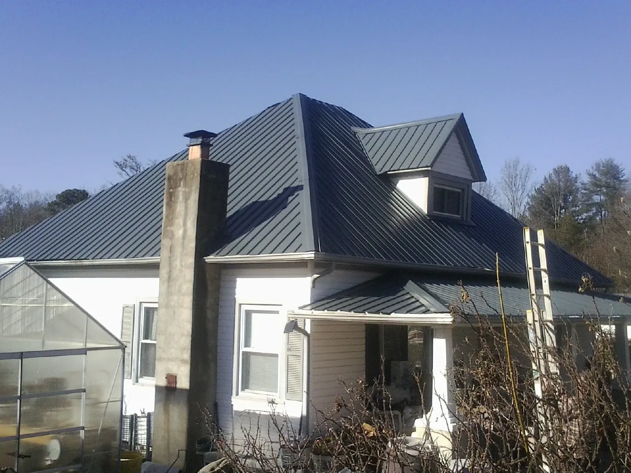 Dark blue standing seam metal roof on a white farmhouse with dormer — Slate & Tile Roof Repair by Roofing Brothers in Rockfield