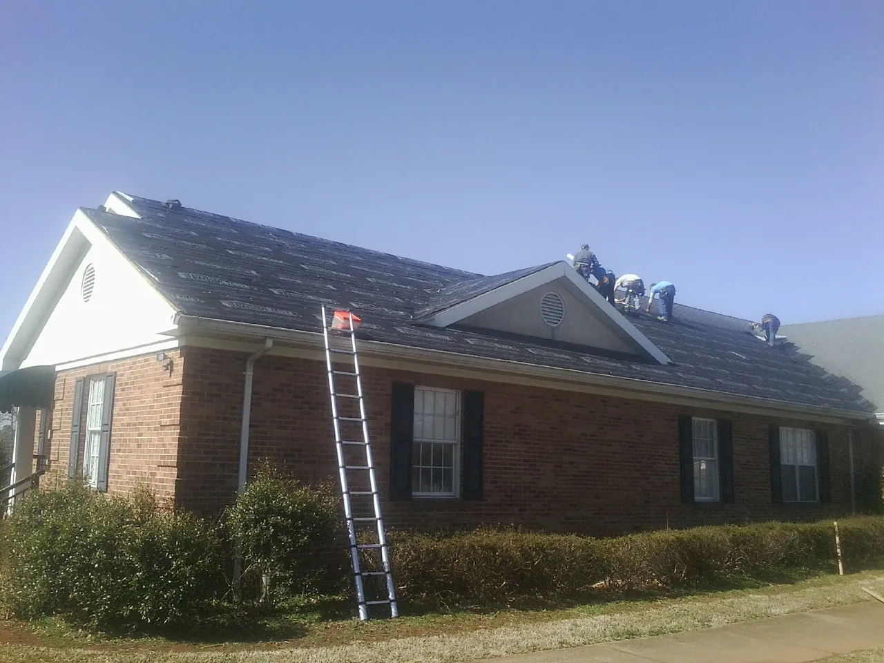 Crew tearing shingles off a brick ranch roof with a ladder set — Emergency Roof Repair work by our crew in Rockfield