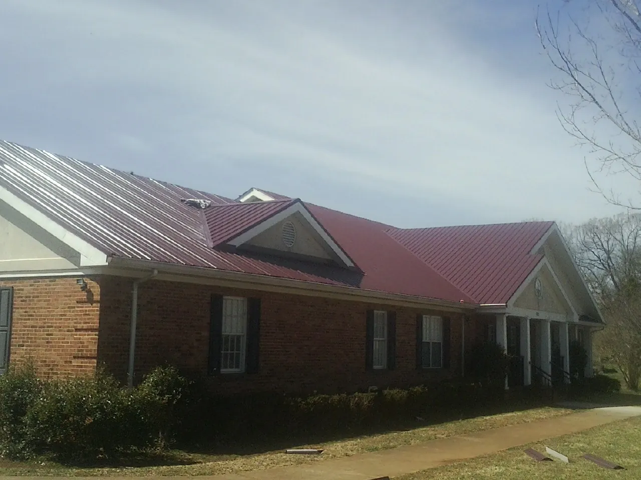 Red metal roof with gabled entries on a long brick building, from a Hail Damage Roof Repair job in Rockfield