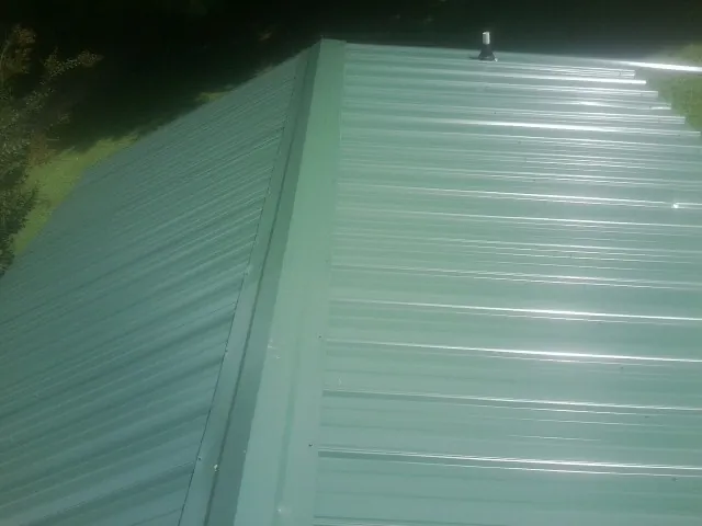 New green metal panels meeting at the ridge of a roof — Flat Roof Repair work by our crew in Rockfield