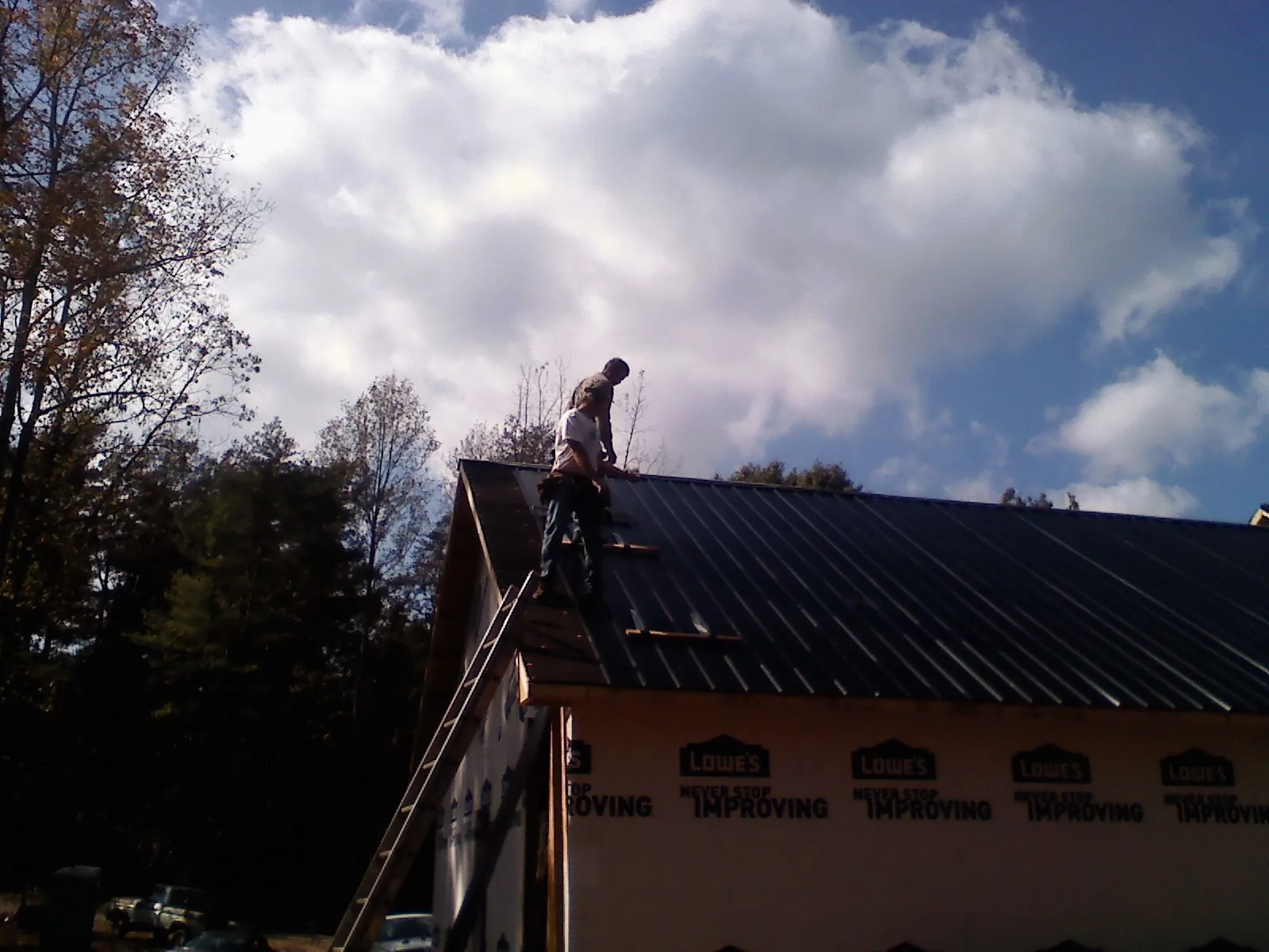 Roofer fastening dark metal panels high against a cloudy sky, from a Roof Inspection job in Rockfield