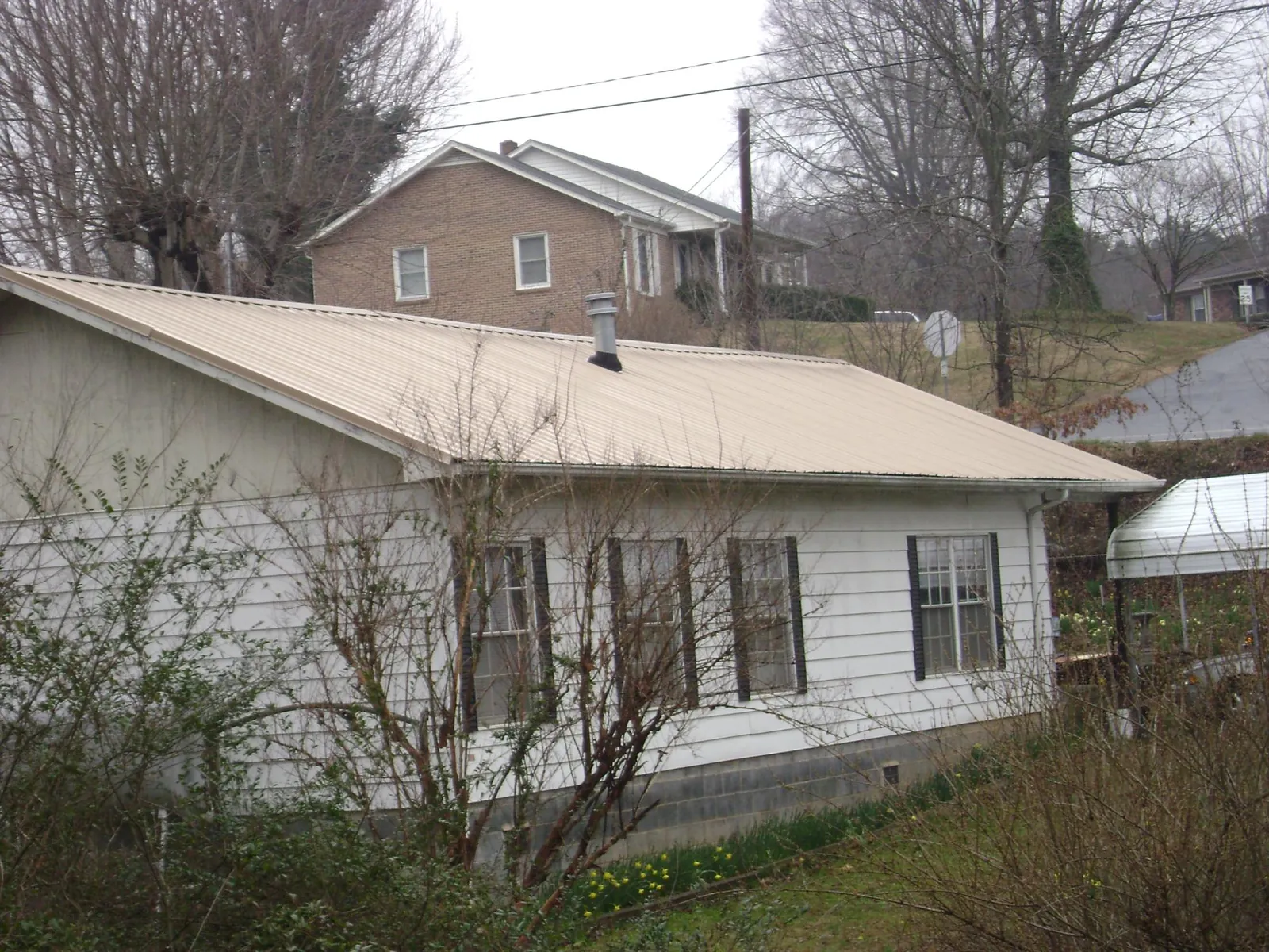 Tan metal roof on a white sided house set into a hillside — Commercial Roofing by Roofing Brothers in Rockfield